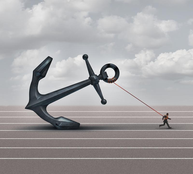 Career burden and business stress concept as a businessman or worker pulling a giant heavy metal anchor as a metaphor for hardship and strugge with taxes or oppression.