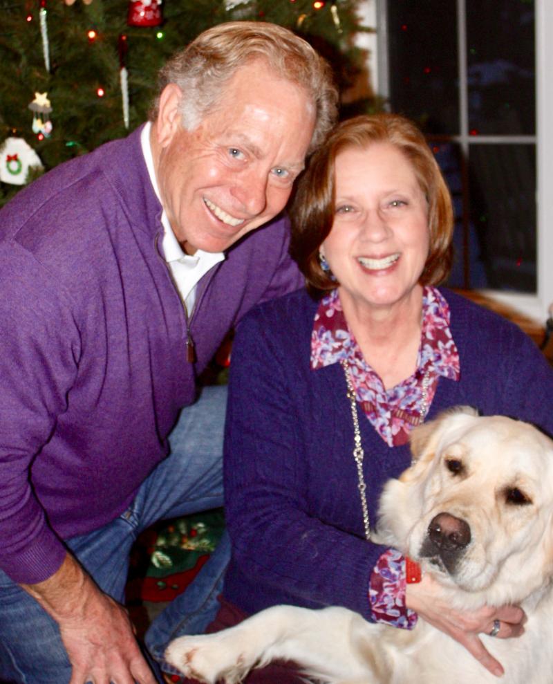 Mike and Nancy McLelland Pose with their dog in front of a Christmas tree.