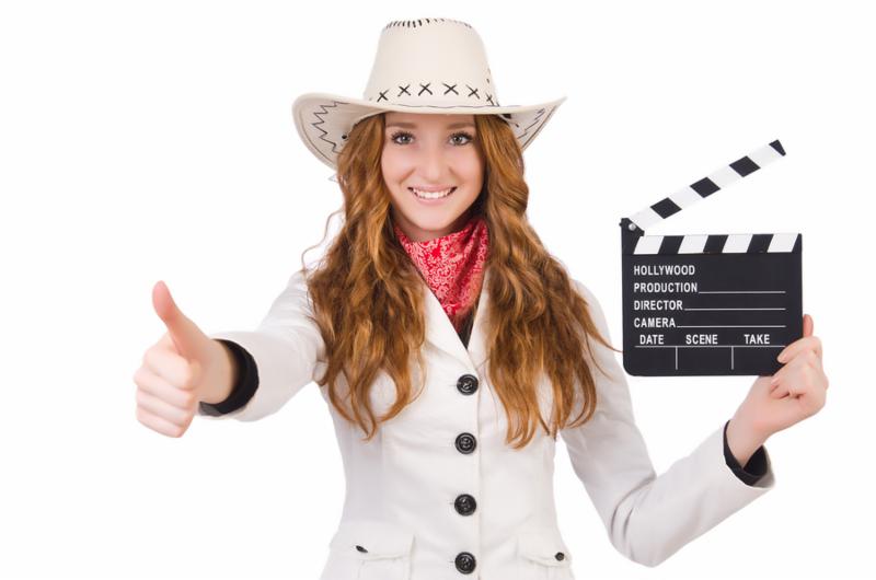 Young  thumbing   cowgirl  with movie board isolated on white
