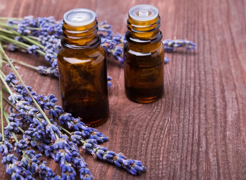Two bottles of aroma oils and lavender flowers on wooden background