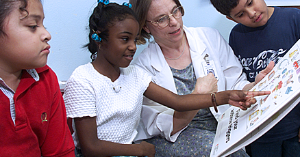  3 children looking at picture book with teacher.