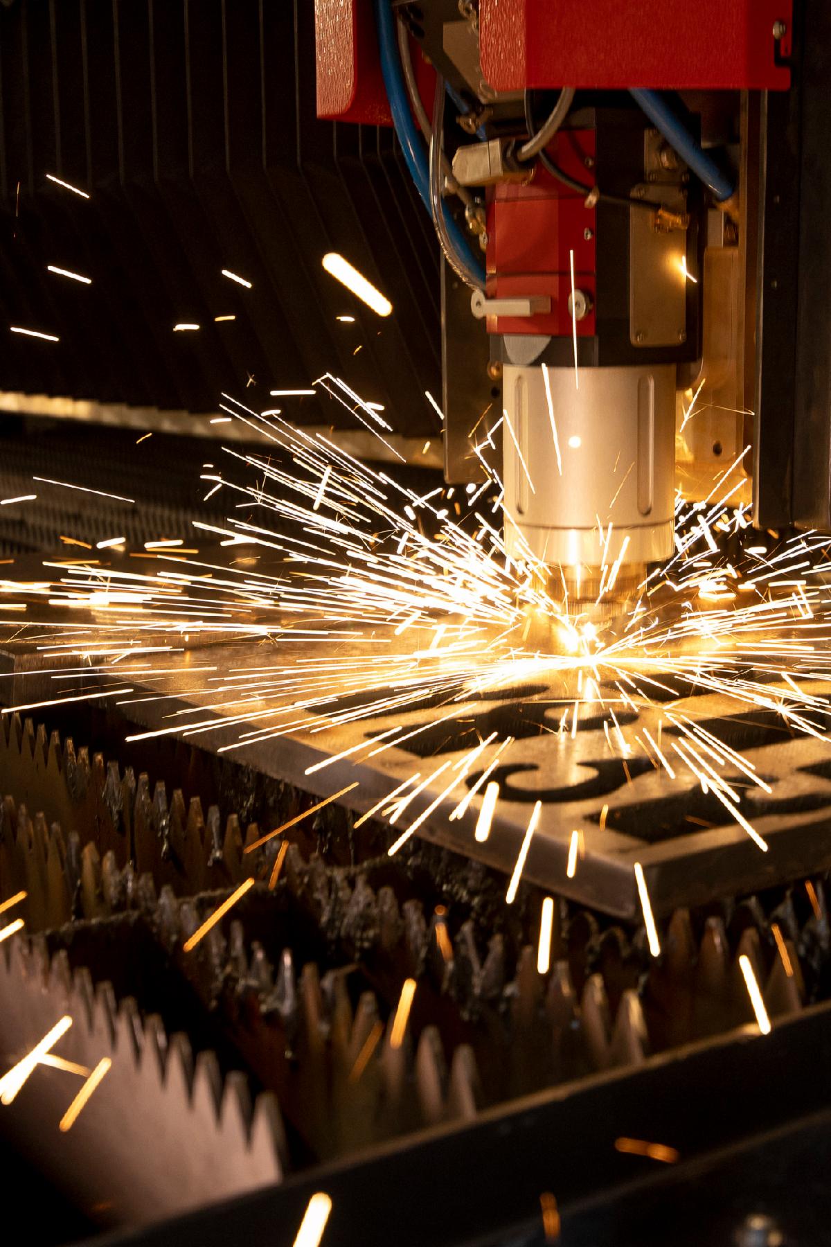 The fiber laser cutting machine cutting the sheet metal plate with the spark light. High tech manufacturing concept.