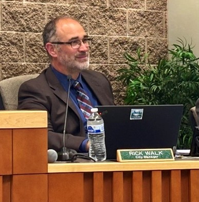A man sitting at a desk with a plant and laptop computer.