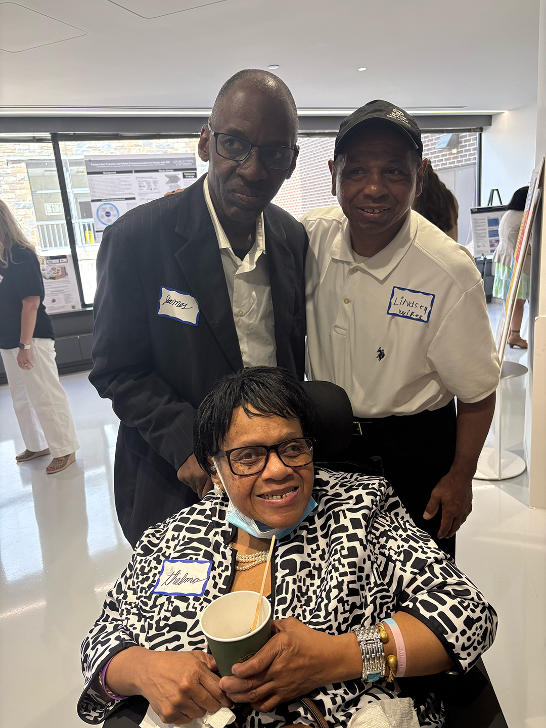 A group of Project ACTION! members smile, 2 men stand with 1 woman in a wheelchair