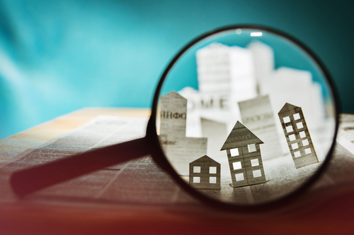 Magnifying glass in front of an open newspaper with paper houses. Concept of rent_ search_ purchase real estate.