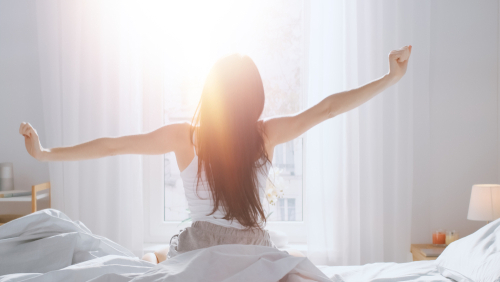 Beautiful Brunette is Waking up in the Morning_ Stretches in the Bed_ Sun Shines on Her From the Big Window. Happy Young Girl Greets New Day with Warm Sunlight Flare.