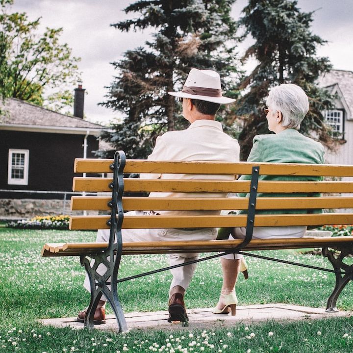 two older adults sitting on bench looking out over field and woods