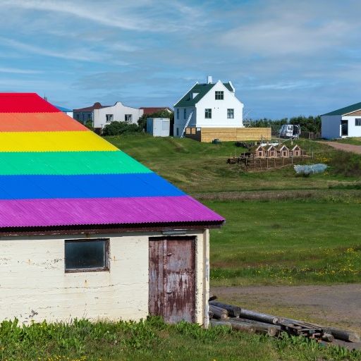 rural homes nestled in hills; barn in foreground features a rainbow painted roof
