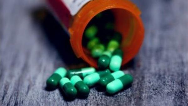 green pills spilling out of pill bottle