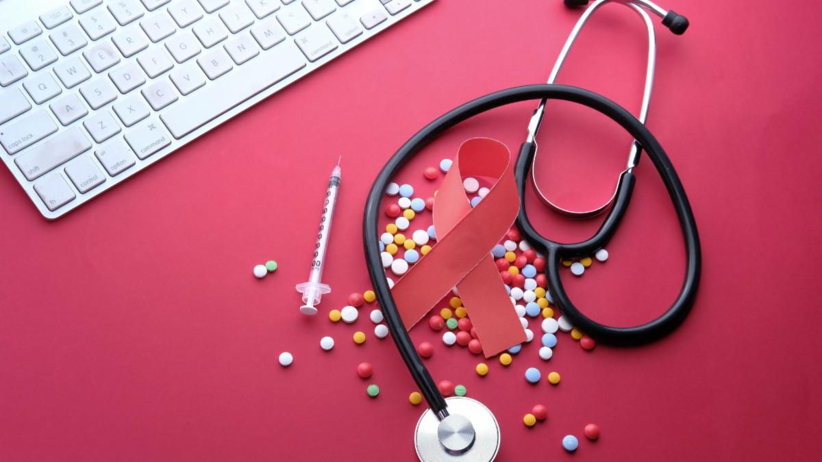 keyboard, red HIV awareness ribbon, stethoscope, pills, syringe, on red background