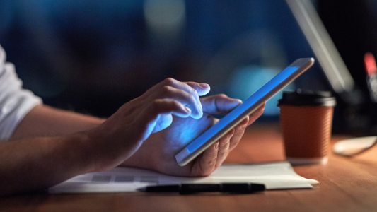 close up of hands holding and tapping on a tablet at desk