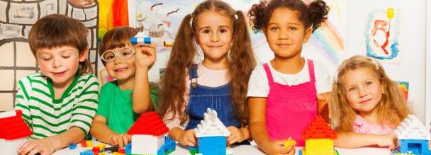Large group of happy kids, boys and girls playing with blocks in kindergarten class constructing simple houses