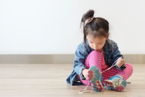 Copy space and Soft focus portrait cute little Asian girl 3 year old sit on the ground and try to tie her shoes. Beautiful kid try to shoelace by herself. concept first step _ growth up and moving on.