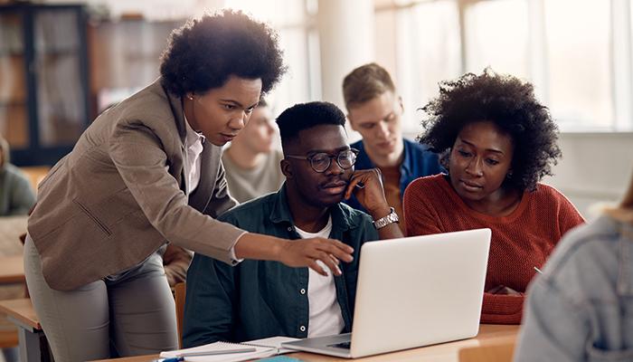 person pointing to laptop to help several other people