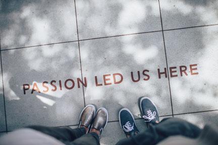 Two pairs of feet on the ground. The words Passion Led Us Here are on the ground.