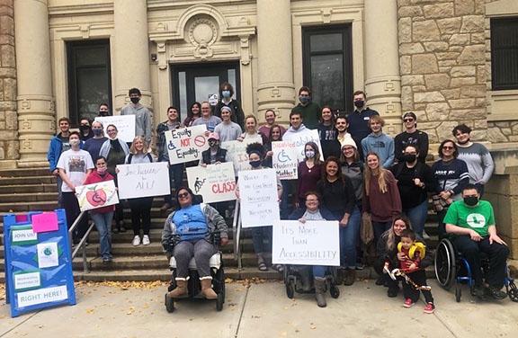 A large group of people gather in front of a building at Washburn holding advocacy signs