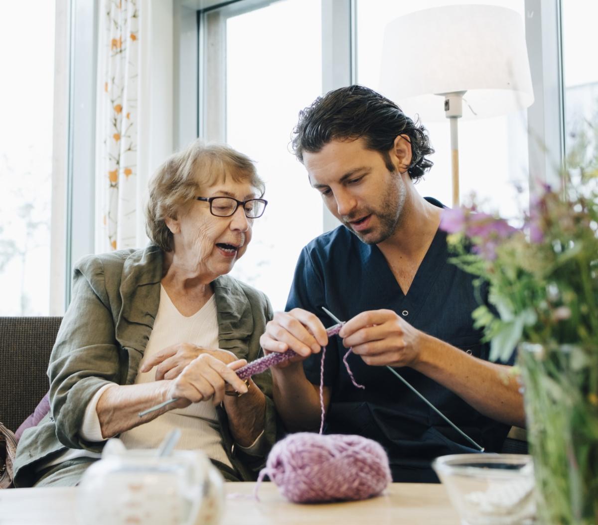 older woman teaching a young male volunteer to knit
