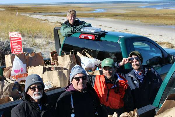 A green pick up truck with bags of food in the back with a handful of people standing around it in warm hats and sunglasses