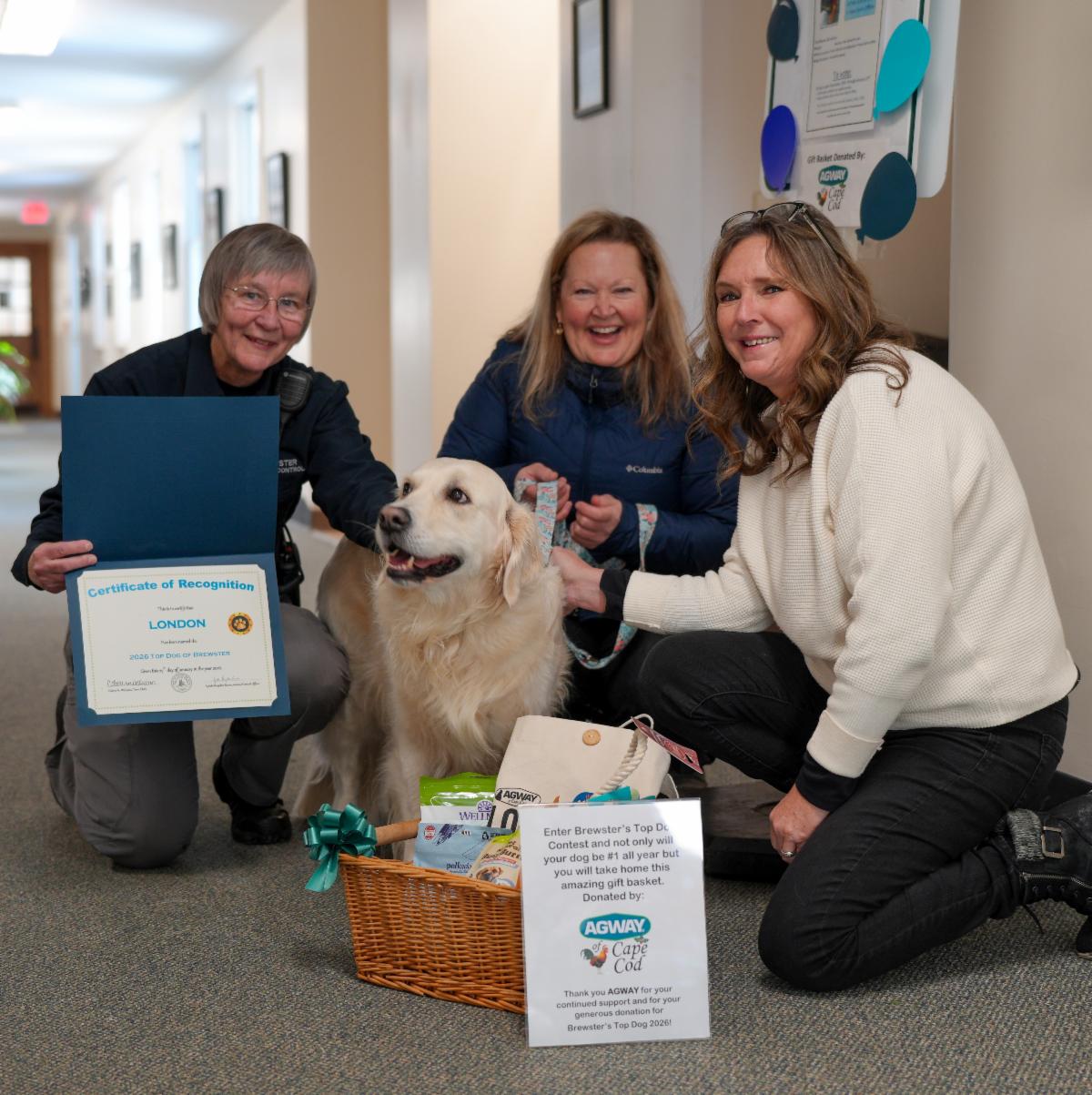 Three people are sitting around a golden retriever everyone is smiling including the dog