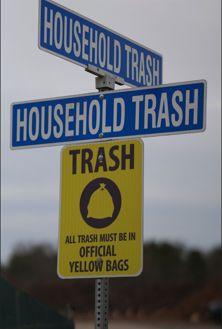 Two blue and white street signs that say household trash with a bright yellow TRASH sign underneath