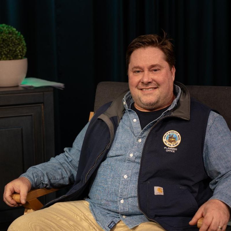 Jon Idman is sitting in a chair and is wearing a brewster zip vest