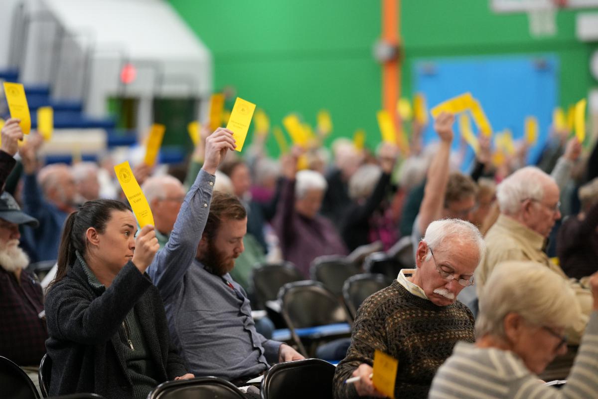 Town meeting picture where residents are lifting yellow voter tags in the air