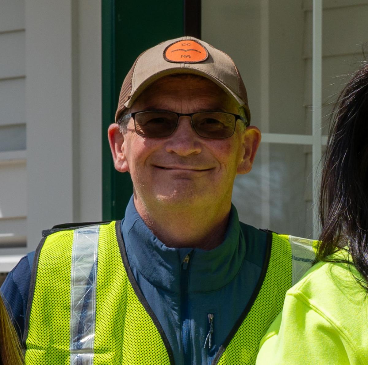 Tom Delaney is wearing a hat sunglass and high viz vest