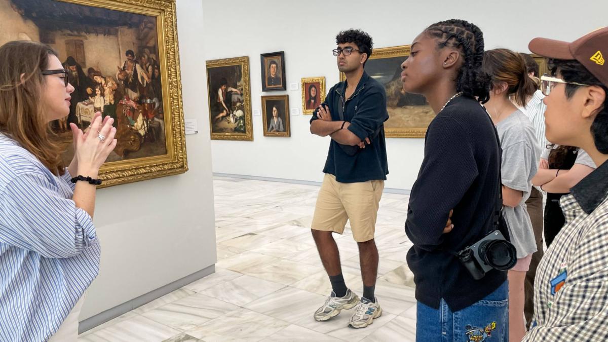 A woman lectures next to a painting while students look on.