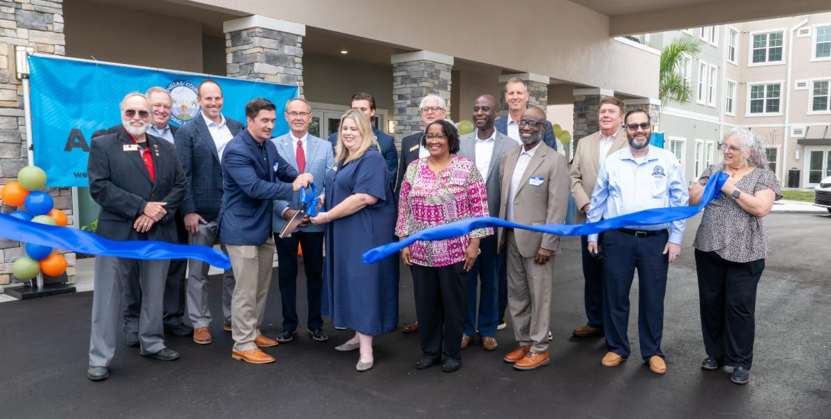 County commissioners and local leaders cut a blue ribbon in front of a new affordable housing building