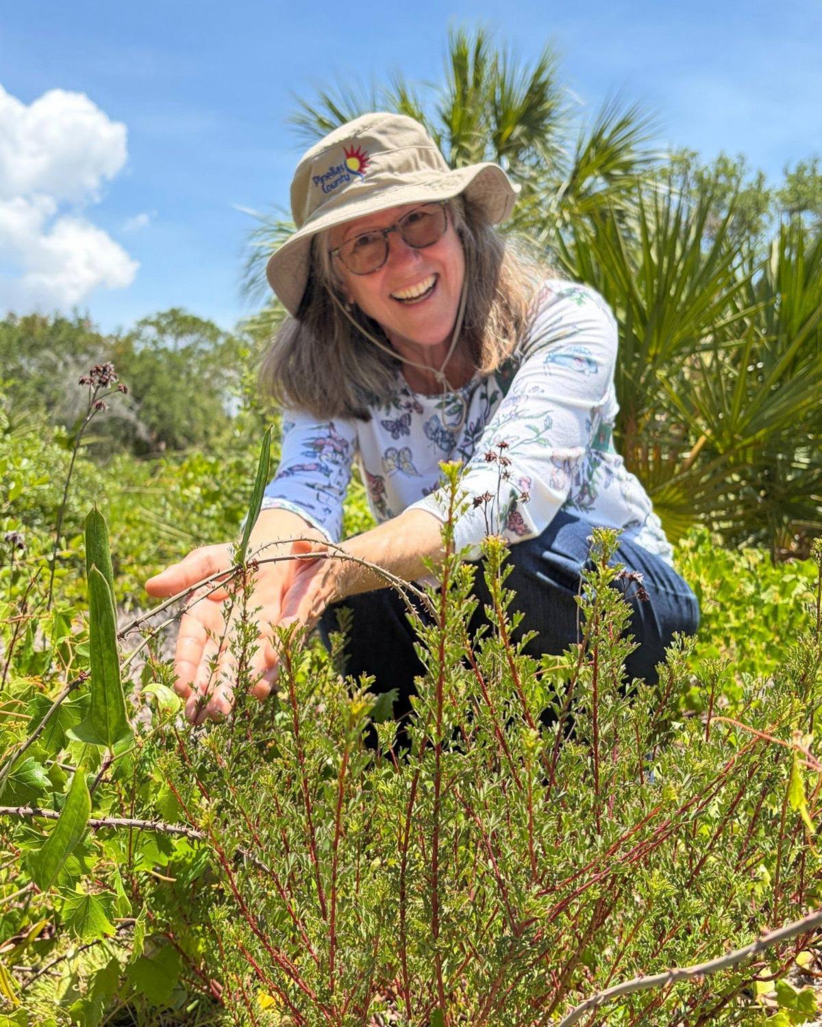 A Pinellas County Parks employee crouches down in a luscious green area and points to new growth.