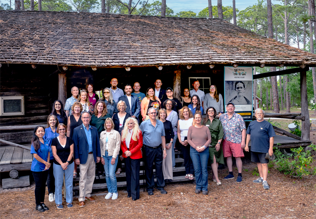 Pinellas County University graduates poses with County staff and leadership in front of cabin at Heritage Village