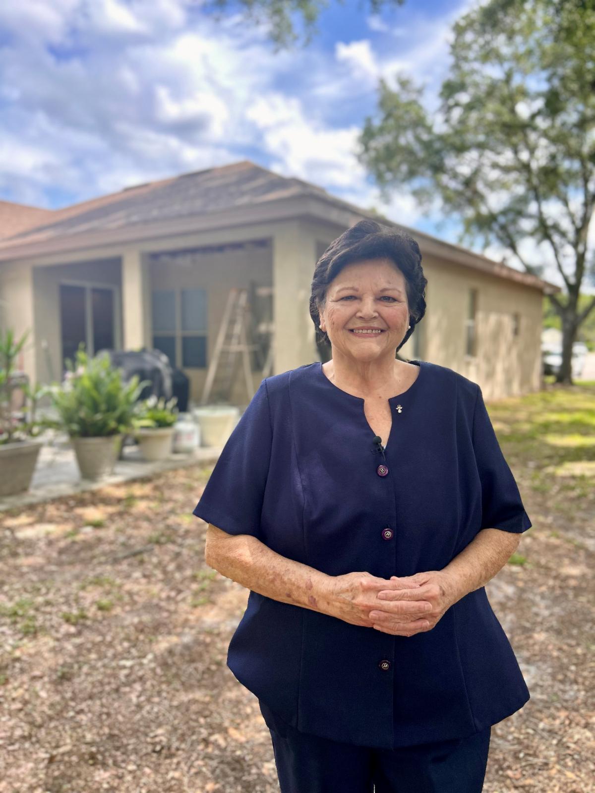 A woman stands in front of her home smiling.