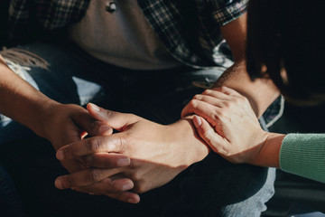 Photo of hands on a lap with another hand consoling the person in distress. Foto de unas manos sobre un regazo con otra mano consolando a la persona en apuros