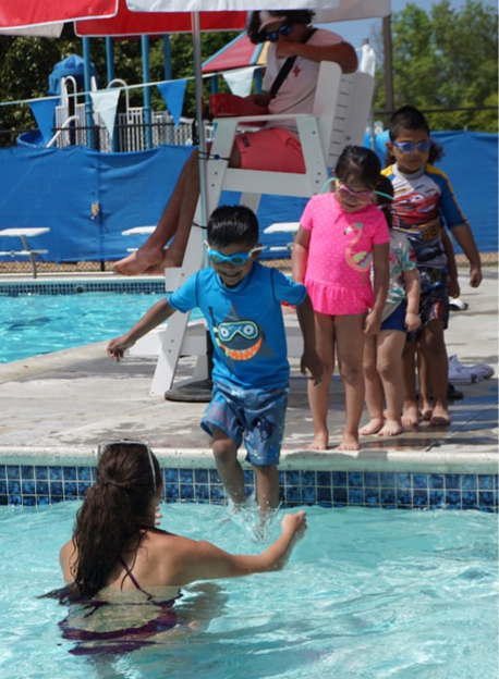 Photo of a woman catching children lined up to jump into a swimming pool