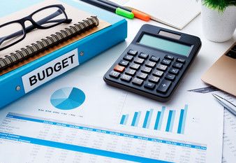 Photo of a budget blue binder with a calculator and other supplies on a desk. Foto de un presupuesto carpeta azul con una calculadora y otros suministros en un escritorio.