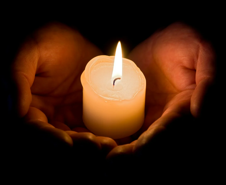 Photo of two hands holding a lit candle