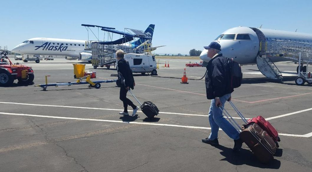 Photo of two Sonoma County Airport passengers unloading from a plane with two aircraft in the background