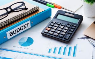 Photo of a budget blue binder with a calculator and other supplies on a desk. Foto de un presupuesto carpeta azul con una calculadora y otros suministros en un escritorio.
