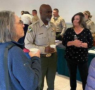 Photo of a group of people speaking with a sheriff inside a building with display tables