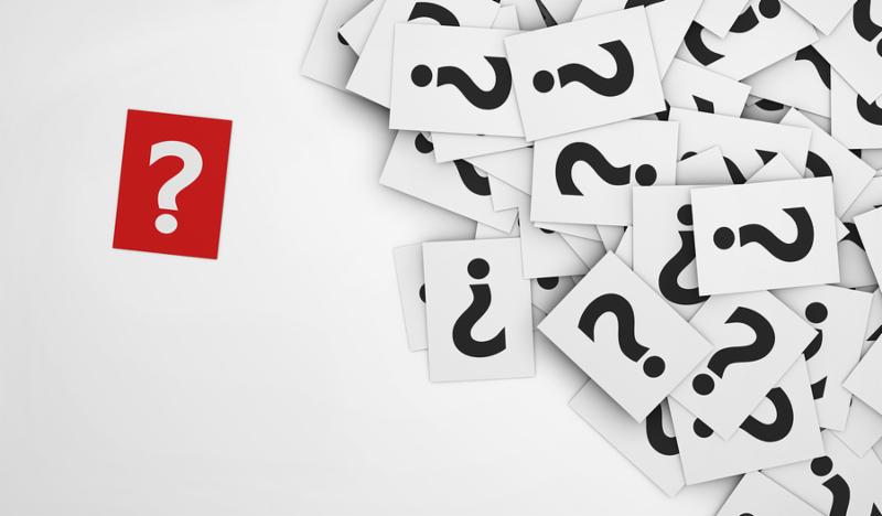 Business questions concept with a question mark symbol on a red paper and a multitude of question marks signs on scattered white papers.