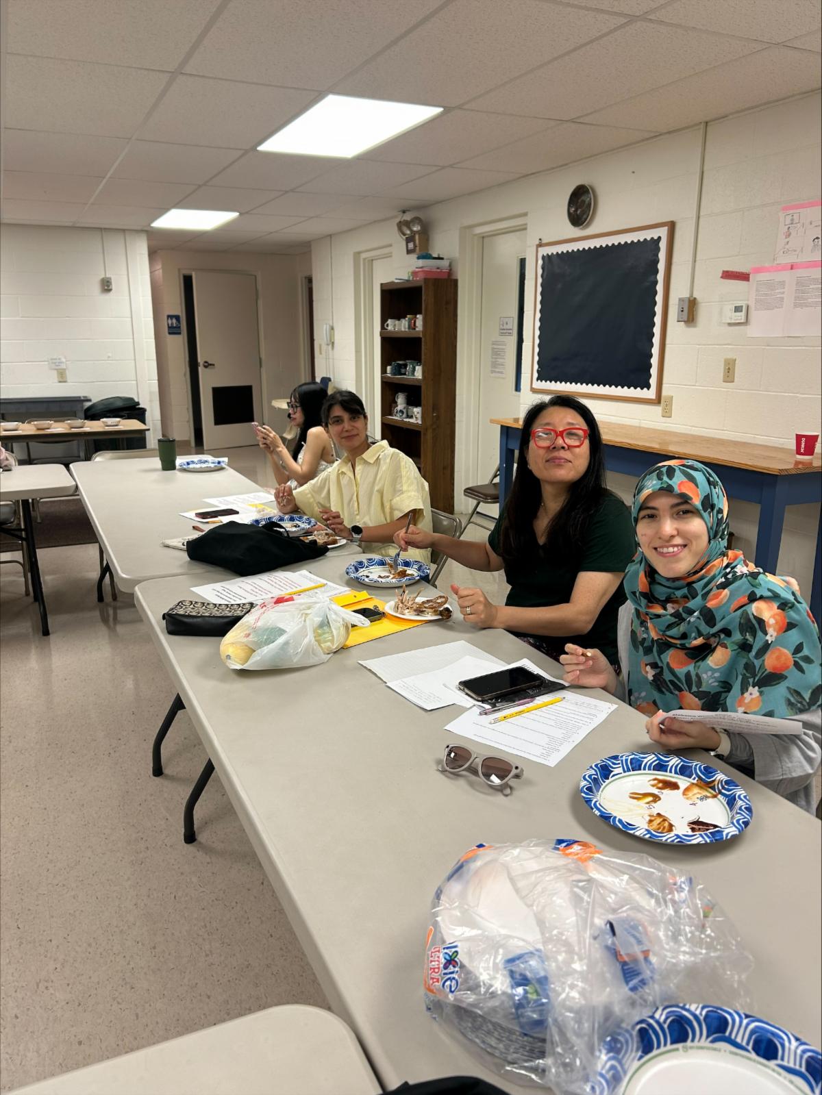picture of several smiling people sitting at a table with papers, plates of food, and other items in front of them