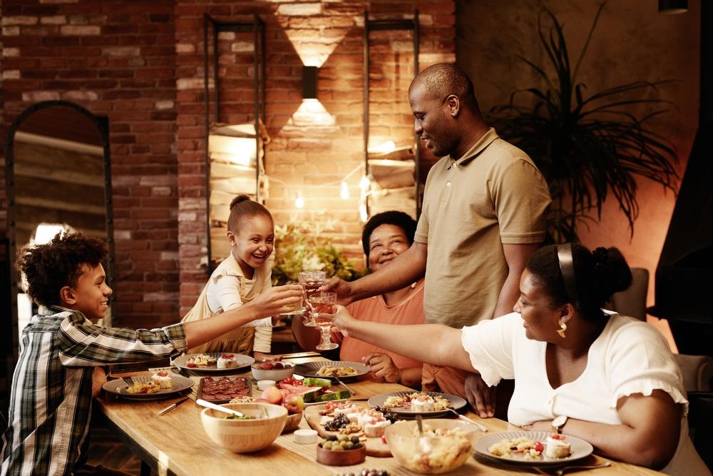 Picture of a family of five at a dinner table, smiling, with food and drink on the table