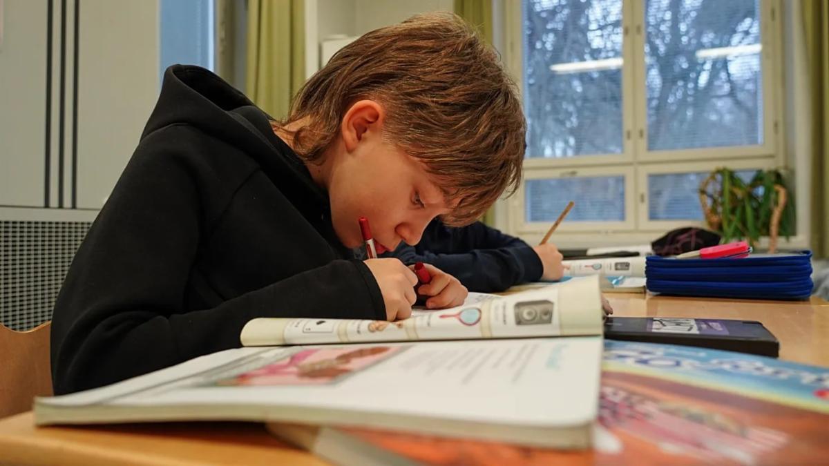 picture of a young boy seated at a table and filling out pages of a workbook