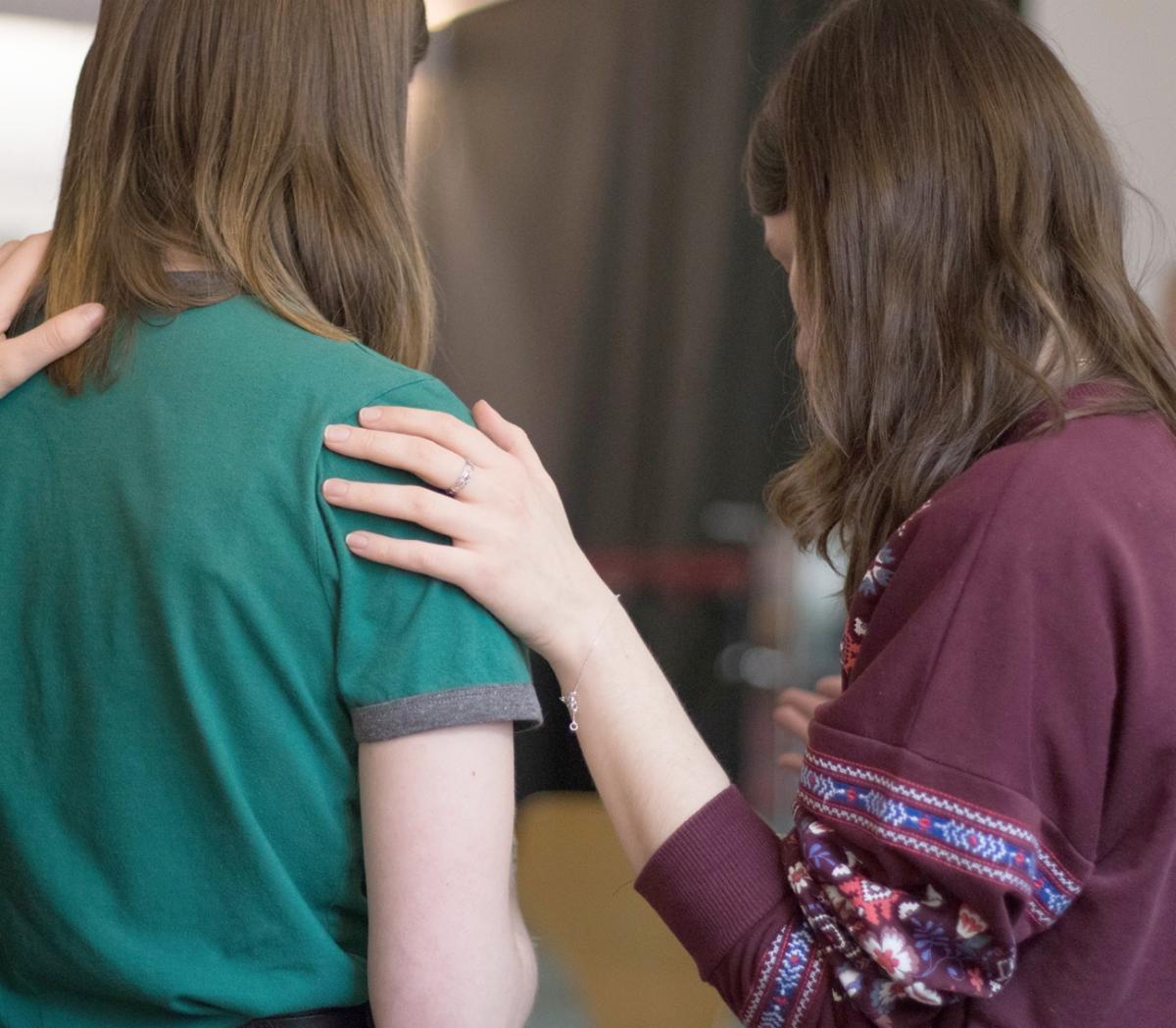 two women standing facing away from the camera one has her hand on the others shoulder