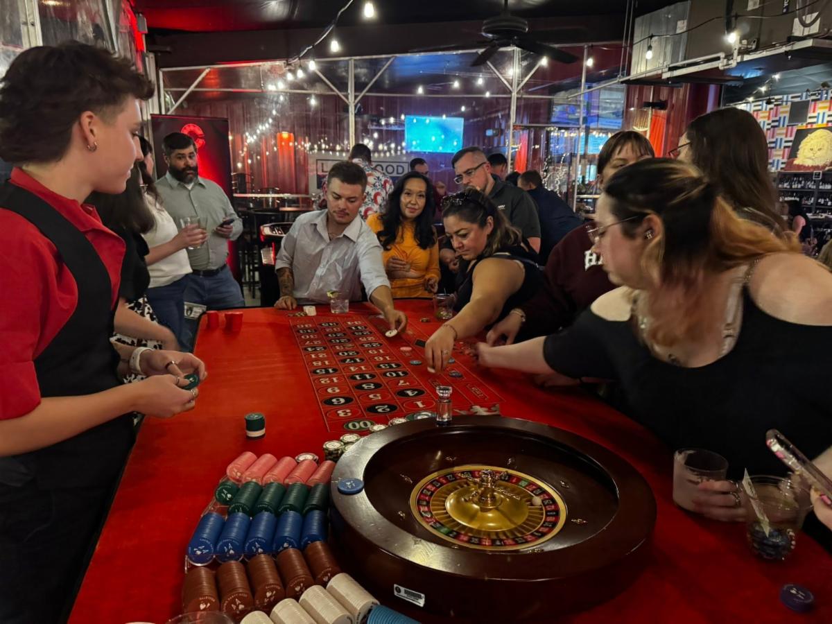A group of people stand around a table playing roulette.