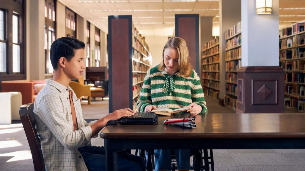 Two disabled students sit at a table in a library.
