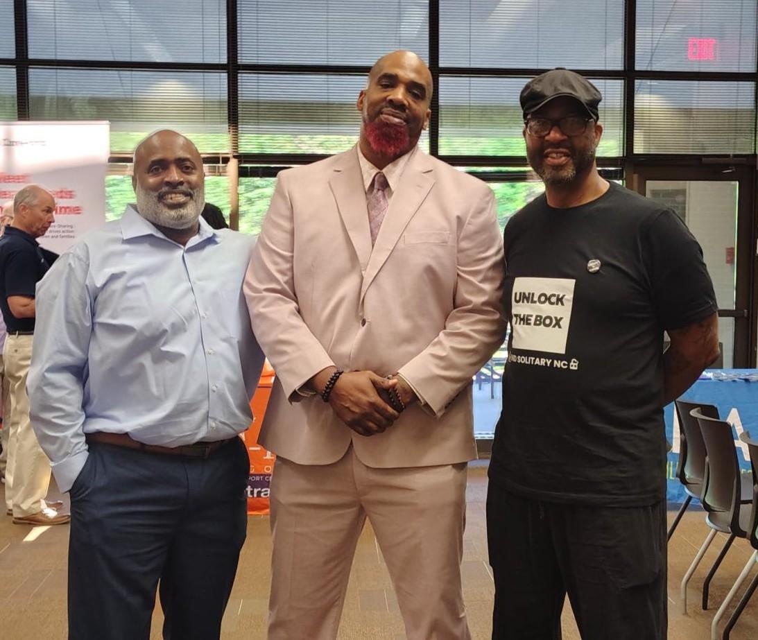 Three black men wearing business attire stand smiling.