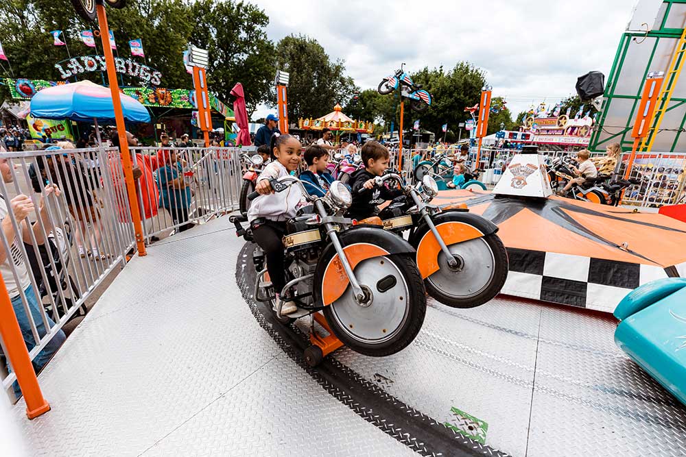 Two children riding a motorcycle ride on the Kidway