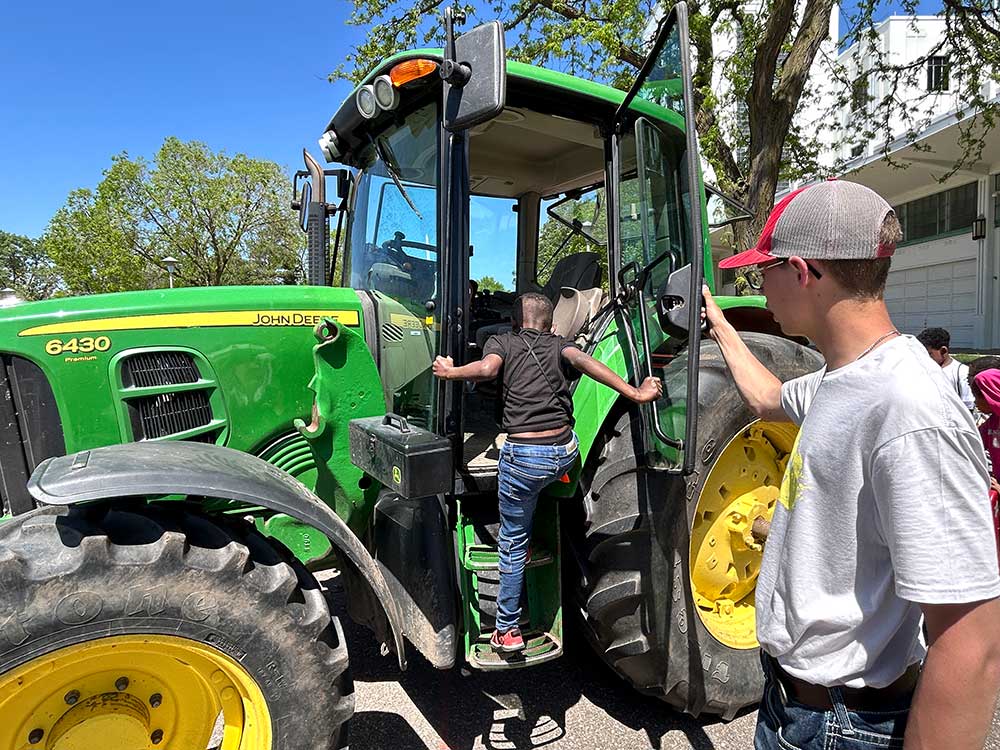 Younger student stepping into a John Deere tractor while and older FFA student holds the door for him