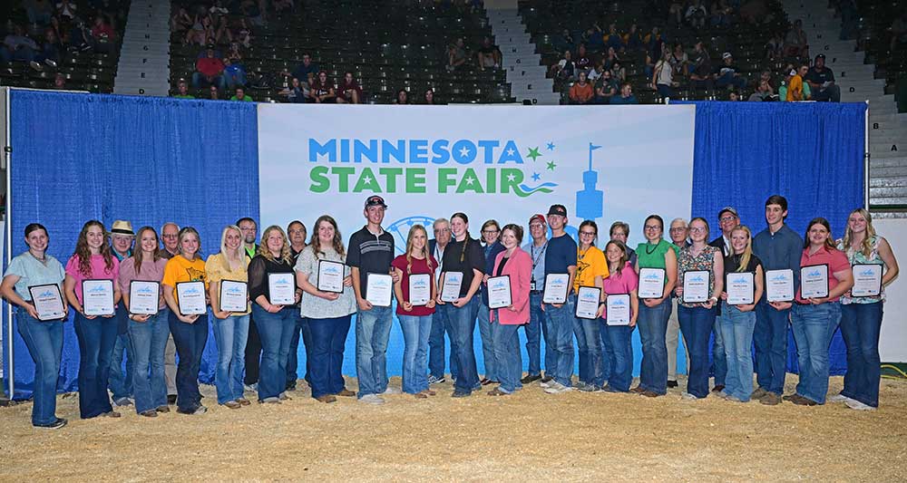 Scholarship award winners holding their certificates for a group photo in front of a blue Minnesota State Fair backdrop.